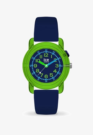 Montre en plastique vert avec un bracelet en silicone bleu marine. Le cadran rond présente des chiffres et des aiguilles bleus sur un fond sombre, avec une couronne en argent.