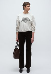 Világos krémszínű pulóver "AMOUR" felirattal, sötétbarna szárban bővülő nadrággal és texturált barna kézitáskával párosítva. Semleges háttér előtt elhelyezve.