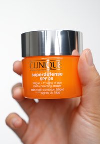 Orange cream jar with silver lid, labeled "Clinique Superdefense SPF 25," designed for multi-correction of fatigue and aging signs.