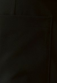 Tela negra con una textura suave, que presenta un bolsillo con costuras rectas y un diseño limpio y minimalista.