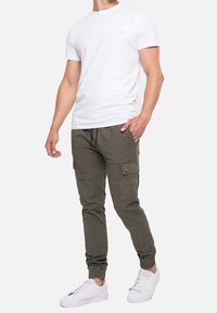 Witte katoenen t-shirt met een ronde halslijn, gecombineerd met olijfgroene cargobroeken met zijzakken en elastische boorden, gedragen met witte sneakers.