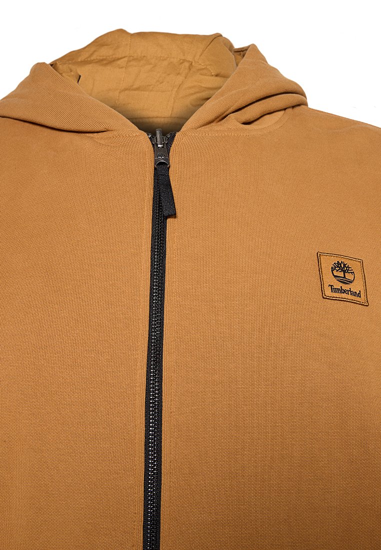 Felpa con cappuccio in tessuto beige con superficie testurizzata. Presenta una cerniera nera e un piccolo logo Timberland nero sul petto.