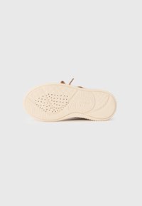 Semelle de chaussure de couleur beige unie, avec des motifs texturés pour l'adhérence et des trous de ventilation pour la respirabilité. Aucune marque ni logo visible.