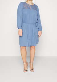 Modré šaty s krajkovým korzetem, nabíraným pasem, dlouhými rukávy a stahovací šňůrkou. V kombinaci s průhlednými sandály na podpatku. Hladká textura látky.