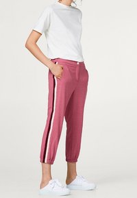 Roze joggers met manchet en zijstrepen, met een ontspannen pasvorm en zakken. Gecombineerd met een effen wit T-shirt met korte mouwen en witte schoenen.