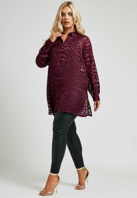 Burgundyröd genomskinlig blus med zebramönster, långa ärmar, knäppning framtill, kombinerad med svarta leggings i konstläder och guldiga klackar med remmar.