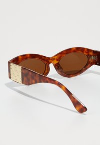 Tortoiseshell sunglasses with brown lenses, pronounced cat-eye shape, and a textured cream accent on the temples.
