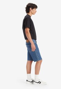 Tricou negru cu mânecă scurtă, pantaloni scurți din denim albastru, adidași albi cu accente negre și șosete albe. Pantalonii scurți au un design cu un buzunar la spate.