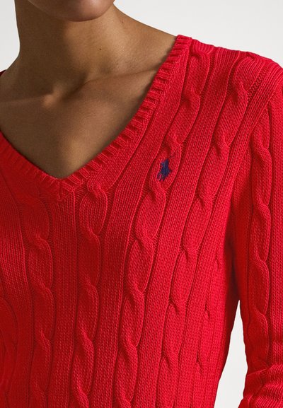 Piros kötött pulóver V-nyakkivágással, bordázott textúrával és kötött mintával, a mellrészen kis tengerészkék logóval.