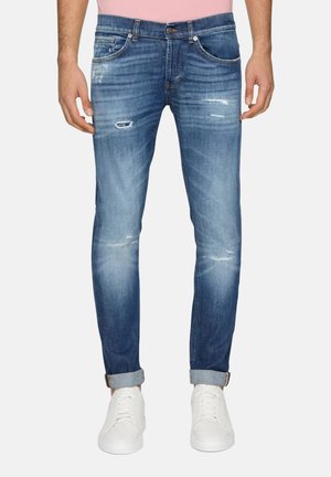 Jeans in denim blu con vestibilità slim, dettagli scoloriti, effetti di sfumatura e orli arrotolati, abbinati a sneaker bianche.