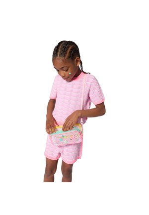 T-shirt en tricot rose avec motif ondulé, associé à un short rose. Porte un petit sac transparent avec des imprimés colorés et une sangle jaune.