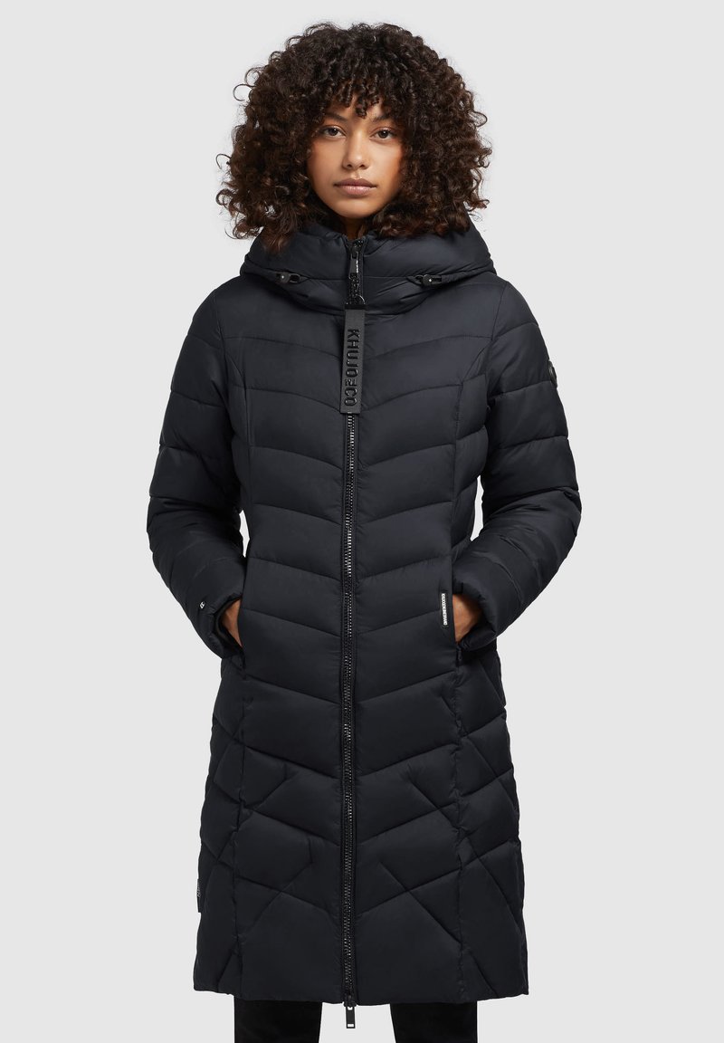 Manteau long noir rembourré avec un motif en chevrons, capuche et fermeture éclair à l'avant. Comprend des poches et un logo sur la tirette de la fermeture éclair.
