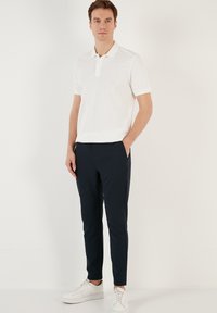 Bílá polokošile s dvoubotkovou légou, kombinovaná s námořnickými slim-fit kalhotami a bílými teniskami. Hladká tkanina, minimalistický design.