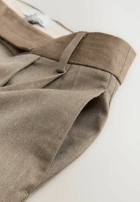 Pantalones marrones con pliegues hechos de una tela texturizada. Presentan una cinturilla ancha y un sutil patrón de rayas. Costuras limpias a lo largo de los bordes.