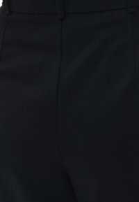 Zwarte pantalon van gestructureerde stof, met een gladde tailleband en plooi details. Ontworpen voor een aansluitende pasvorm.