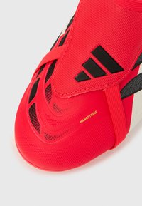 Εγγύς λήψη ενός κόκκινου ποδοσφαιρικού παπουτσιού Adidas Nanostrike με μαύρες λεπτομέρειες και υφή συνθετικού άνω μέρους.