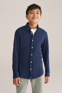 Tums zilas garām piedurknēm krekls, izgatavots no mīksta auduma, ar pogām pie apkakles, baltām pogām un smalku logo uz krūtīm.