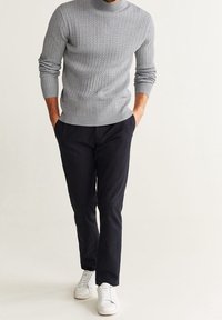 Jersey de cuello alto gris con canalé y mangas largas, combinado con pantalones ajustados oscuros y zapatillas blancas de caña baja. Diseño sencillo y moderno.