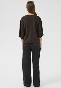 Braunes, übergroßes T-Shirt mit gesenkten Schultern, kombiniert mit lockeren, dunkelblauen Jeans aus Denim mit subtilen Nähten und hohem Bund.