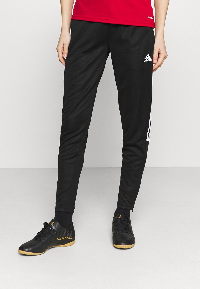 Černé sportovní kalhoty s bílými bočními pruhy a elastickým pasem, spárované s černými teniskami se zlatými akcenty.