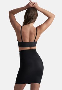 Top corto aderente nero e gonna alta in vita, realizzati in materiale liscio, con spalline sottili e design minimalista.