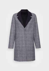 Cappotto singolo petto in bianco e nero a motivo houndstooth, con colletto a rever nero e tasche frontali, esposto su uno sfondo bianco.