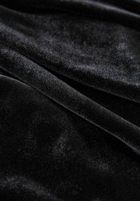 Tejido de terciopelo negro con una textura suave y lisa, pliegues visibles y reflejos de luz que destacan su rica profundidad y superficie mullida.