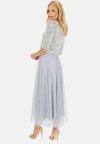 Srebrna bluzka z cekinami i rękawami o długości trzech czwartych, zestawiona z lekko niebieską, zwiewną spódnicą z tiulu oraz cielistymi szpilkami.