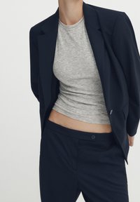 Navy tailored blazer over a light gray fitted t-shirt, paired with matching navy trousers. The fabric appears smooth with structured design elements.