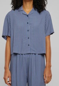 Camisa de manga corta a rayas azules con cuello, dobladillo redondeado y cierre frontal de botones. El material parece ligero y suave.