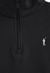 Sudadera negra con cremallera y cuello alto, con un pequeño emblema blanco de golfista en el lado izquierdo del pecho y un acabado de tela texturizada.