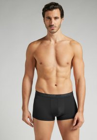 Schwarze Boxershorts aus glattem Stoff mit einem elastischen Bund, der den Markennamen trägt. Enganliegendes Design, minimalistischer Stil.