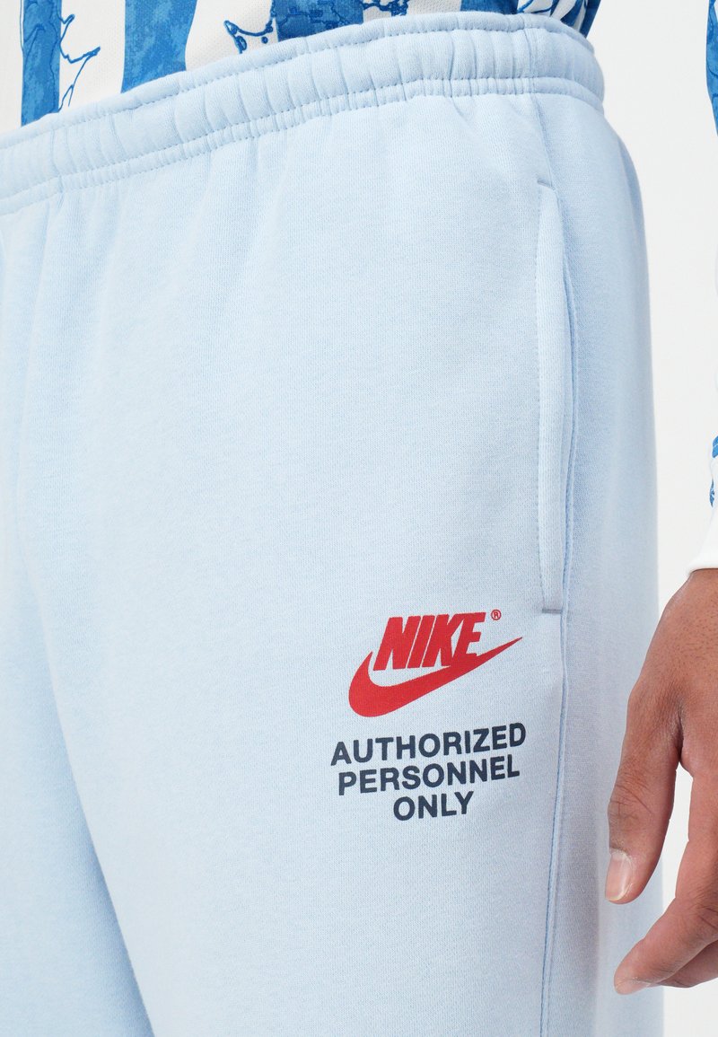 Helle blaue Nike-Sweatpants aus einem Baumwollmix, mit einem roten Logo und schwarzem Text „NUR FÜR AUTORISIERTES PERSONAL“ an der Seite.
