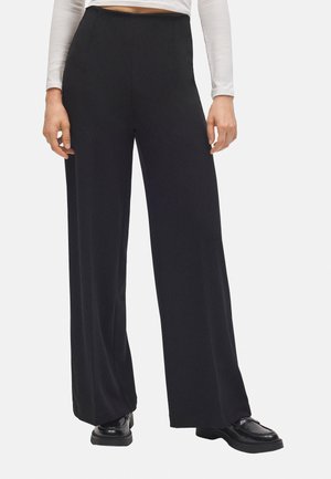 Pantalones de pierna ancha negros y fluidos, confeccionados con una tela suave, con una cintura ajustada y un diseño minimalista, combinados con zapatos negros gruesos.