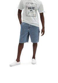 T-shirt grigio chiaro da uomo con logo Vans nero, abbinato a pantaloni corti di jeans blu e scarpe slip-on bianche. I pantaloni corti di jeans presentano tasche laterali.