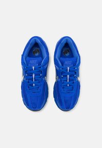 Plave Nike tenisice s mrežastim gornjim dijelom, vezicama i srebrnim detaljima. Imaju teksturiranu jezičak i logo na unutarnjoj strani. Dizajnirane za udobnost i prozračnost.