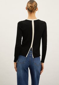 Black sweater with a contrasting cream back seam. Features a round neckline and long sleeves, made of a smooth knit fabric.