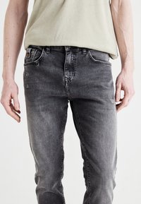 Jeans in denim nero sbiadito con taglio dritto, dotati di cinque tasche, chiusura con bottone metallico e leggera abrasione sulle ginocchia.