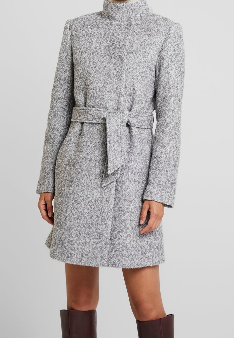Manteau gris longueur genoux en tissu texturé, doté d'un col montant et d'une ceinture assortie nouée à la taille, avec des manches longues.