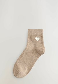 Beige bomullssocka med ribbad krage, dekorerad med ett litet vitt hjärt-mönster på sidan. Slät textur, ankellängd.
