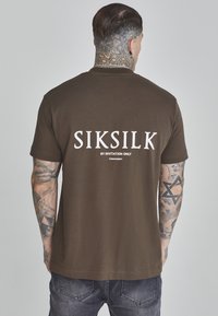 Camiseta de algodón marrón con un gran logo blanco "SIKSILK" en la parte posterior. Manga corta, corte estándar y una textura suave.