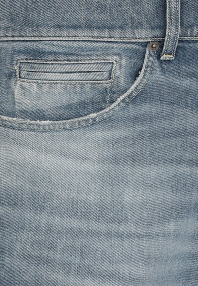 Tessuto denim blu chiaro con una tasca posteriore e cuciture visibili, leggermente sfilacciata, texture morbida e un sottile motivo sbiadito.