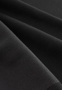 Zwarte stof met een glad, gestructureerd oppervlak, met fijne ribbels en een gelijkmatig weefpatroon. Het materiaal is gevouwen, waardoor zachte contouren ontstaan.