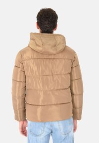 Giacca a vento beige con cappuccio, caratterizzata da una superficie liscia e lucida, cuciture orizzontali e polsini elasticizzati. Vista da dietro.