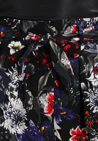 Floral skirt featuring a black background with colorful red and white flowers. It has a wide waistband and a fabric tie at the front.