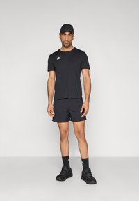 Čierne športové tričko a šortky, obe z ľahkej látky. Čierna čiapka a topánky, na tričku a ponožkách biele logá.