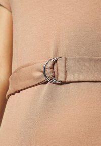 Robe pêche pâle en tissu texturé. Elle présente une large ceinture avec une boucle circulaire argentée et un détail de nœud à la taille.