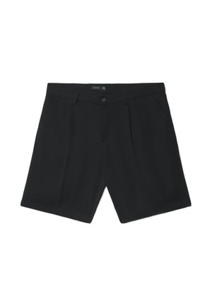 Schwarze, maßgeschneiderte Shorts mit vorderen Falten, Knopf- und Reißverschluss, Gürtelschlaufen und Seitentaschen, flach auf einem weißen Hintergrund ausgebreitet.