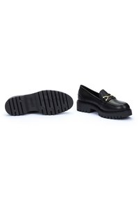 Mocasinés de cuero negro con suela gruesa y estriada; acento de hardware dorado en la parte delantera; textura suave; diseño minimalista.
