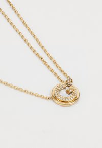 Collier doré présentant un pendentif circulaire avec un accent de strass étincelant et un design de chaîne torsadée.
